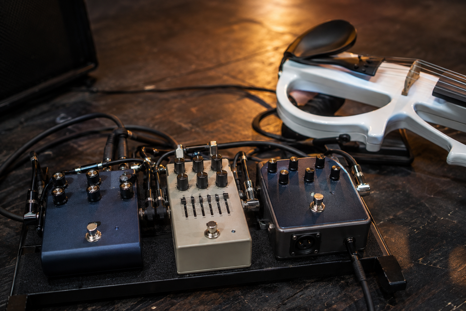 Близък кадър на electric violin pedalboard по време на soundcheck с chorus, EQ и DI педали под топла backstage светлина