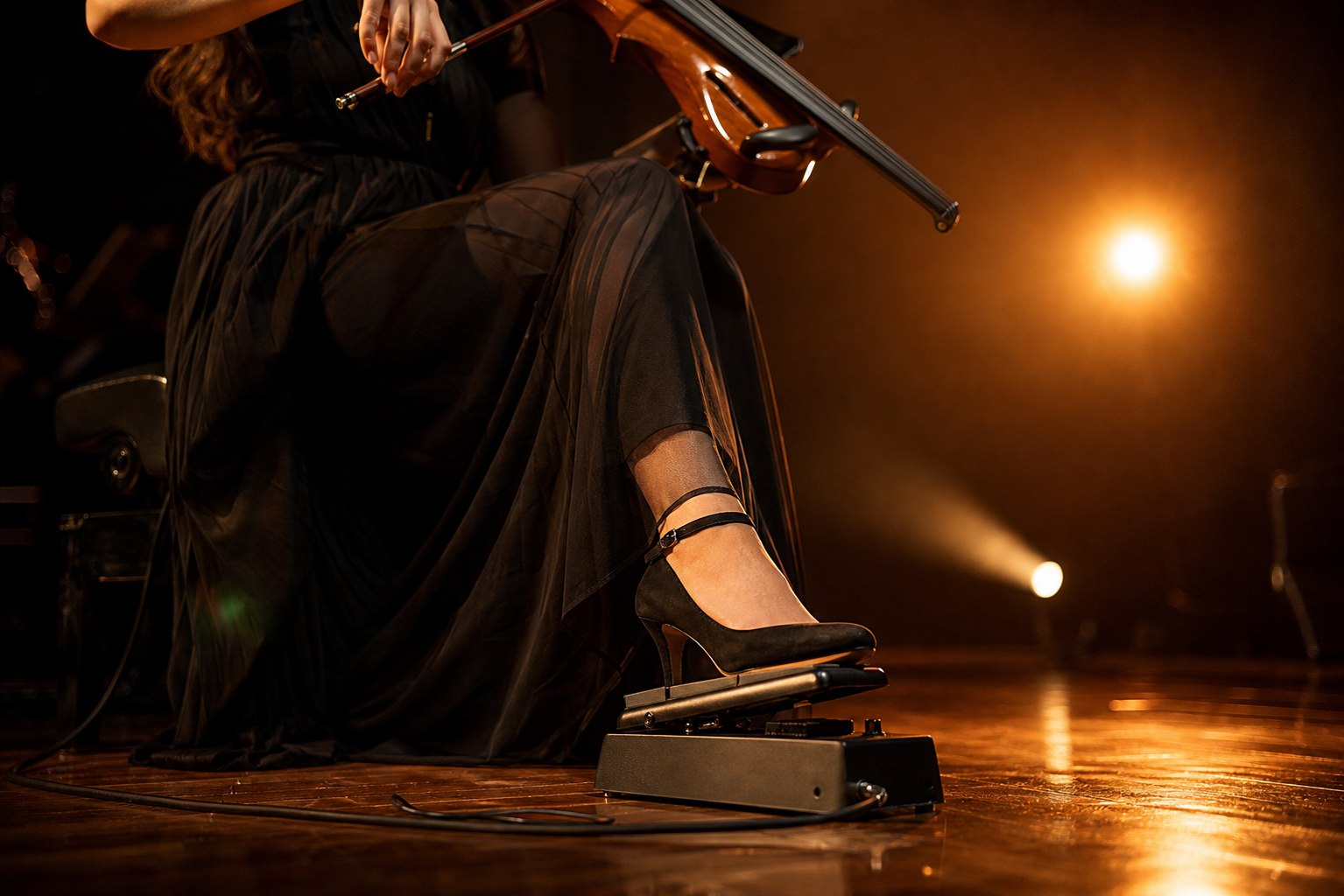 Близък концертен кадър на electric violin изпълнителка, която оформя фразирането с крак върху expression pedal