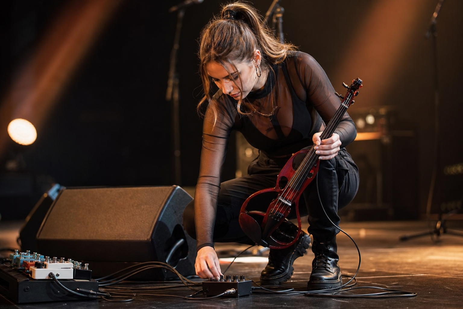 Electric violin изпълнител прави последна pre-show настройка на isolator до pedalboard с подредени кабели на тъмна концертна сцена