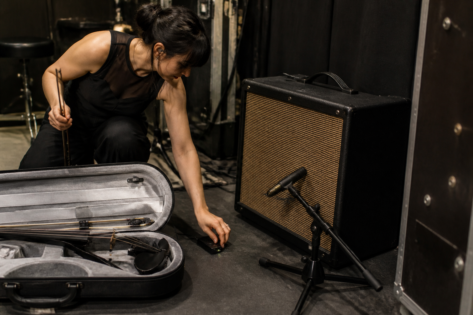 Backstage electric violin setup с ниска short-boom стойка за микрофон, насочена към малък amp до отворен violin case