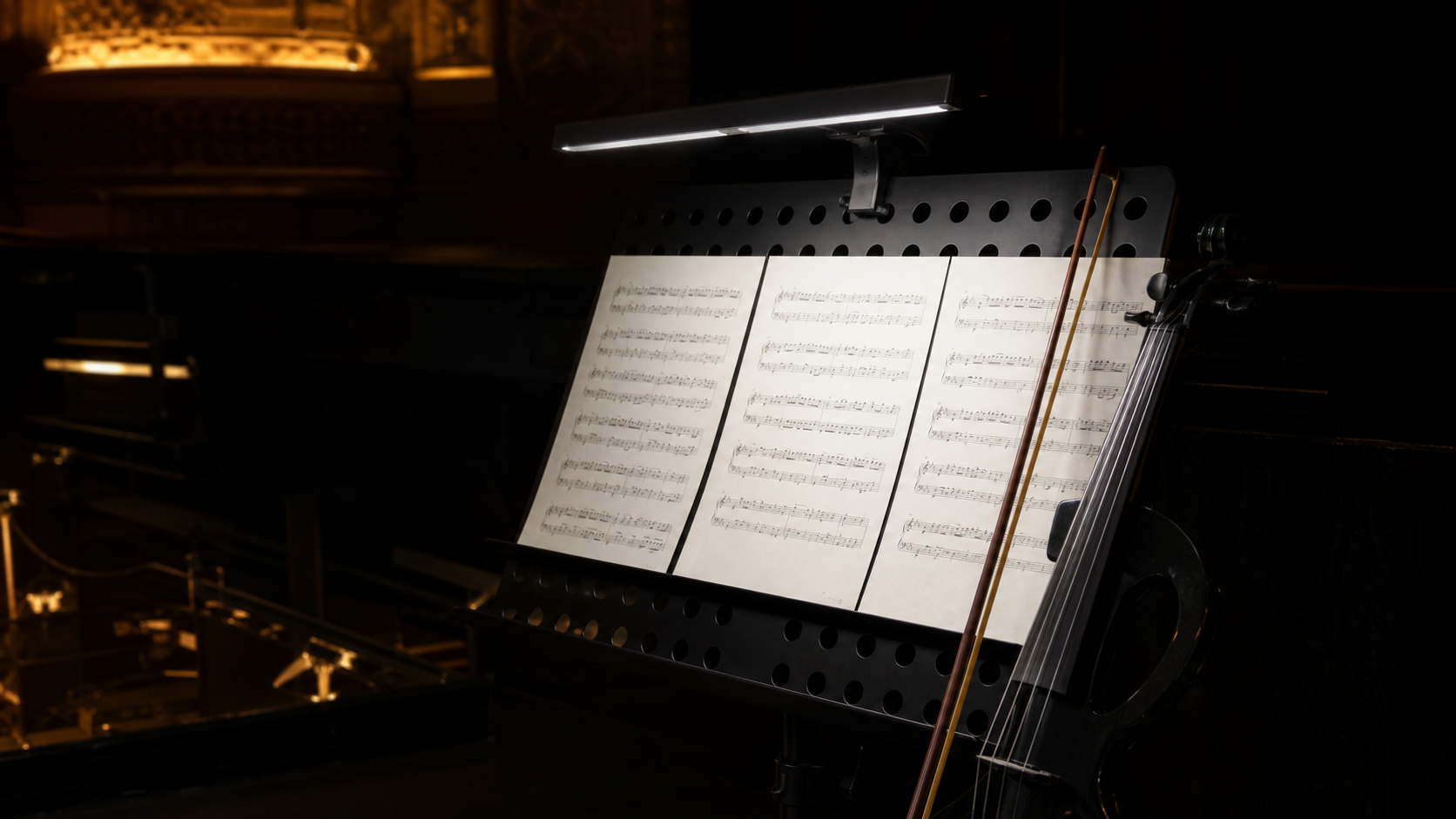Широка clip-on лампа осветява няколко страници на черен нотен пулт до electric violin в тъмна театрална оркестрина