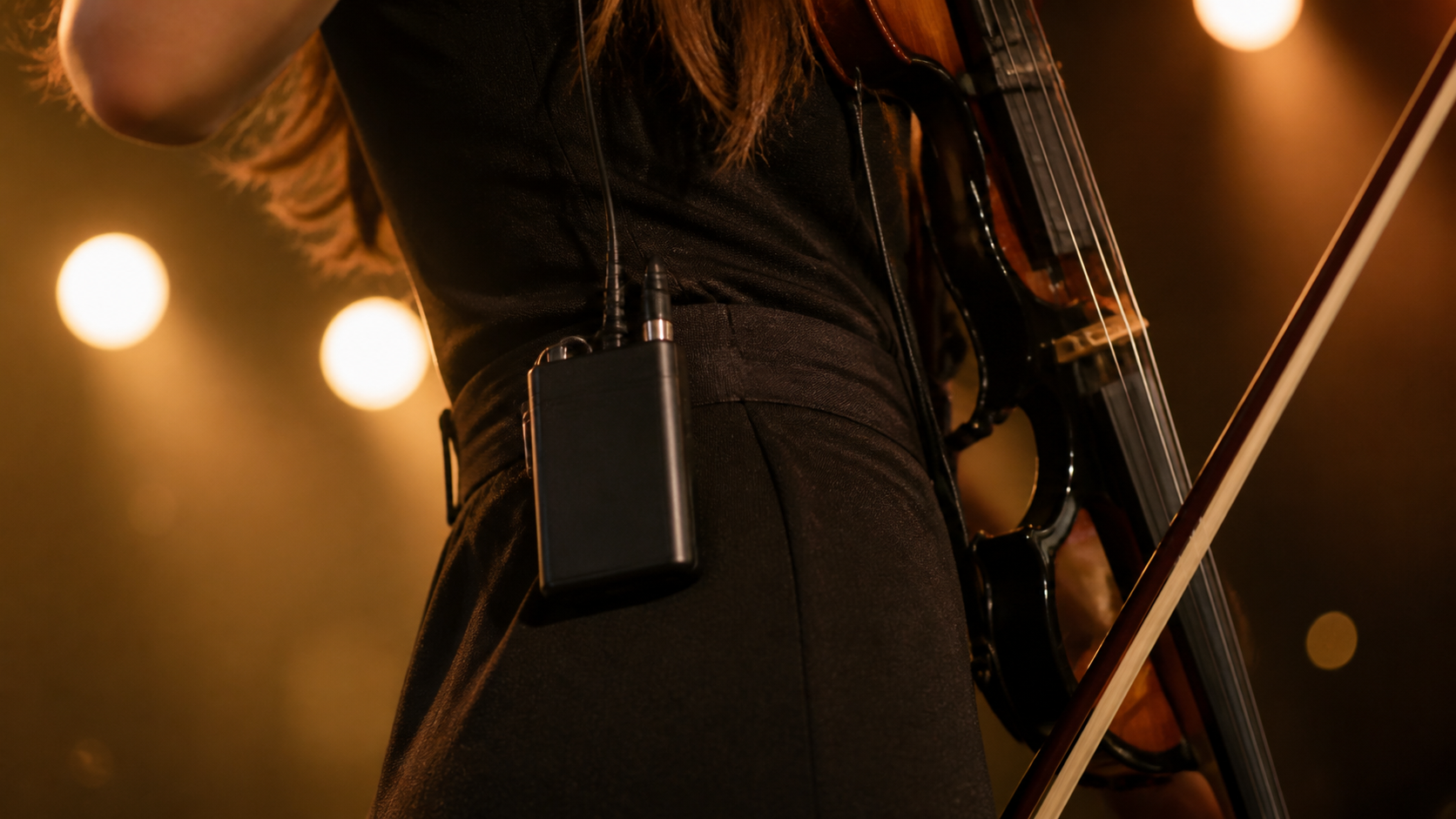 Close-up of wireless in-ear monitor receiver clipped to a performer outfit beside an electric violin during a live show